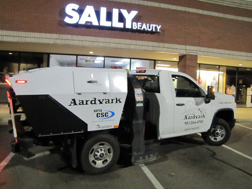 Aardvark sweeping a retail parking lot at night in Memphis